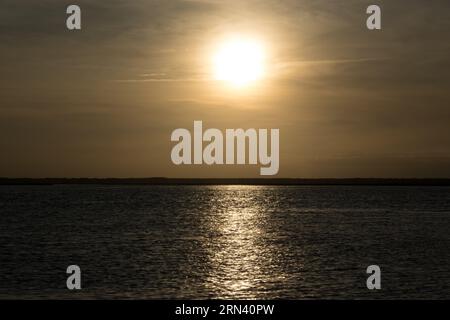 BULLYARD SOUND, South Carolina, USA – Ein lebhafter Sonnenuntergang erleuchtet den Himmel über dem Bullyard Sound in der Lowcountry Region von South Carolina. Das goldene Licht der untergehenden Sonne reflektiert das ruhige Wasser des Gezeitenflusses und erzeugt ein atemberaubendes Farbenspiel über Himmel und Wasser. Silhouetten der Küstenvegetation, wahrscheinlich Spartina-Gras, bilden die Kulisse und zeigen die einzigartige Schönheit dieses Küsten-Ökosystems. Stockfoto