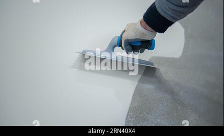 Arbeiter, der einen weißen Eimer aus Epoxidharz auf den Boden aufgibt Stockfoto