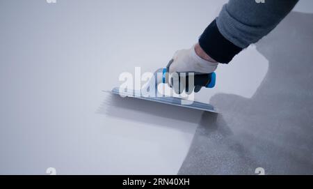 Arbeiter, der einen weißen Eimer aus Epoxidharz auf den Boden aufgibt Stockfoto