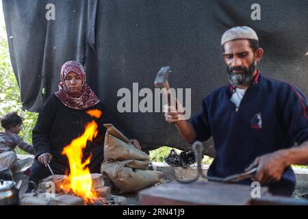 GAZA, 1. Mai 2015 -- die Palästinenserin Aisha Hussein, 36, und ihr Mann Ibraheem Mustafa arbeiten in schmelzenden Stahlstäben in einem kleinen Zelt, das am 1. Mai 2015 an einer Hauptstraße in Gaza-Stadt errichtet wurde. Aisha ist Hausfrau und hat einen der schwierigsten Jobs ausgeübt, um ihrem Mann zu helfen, die schwierige Lebenssituation ihrer Familie zu überwinden. Am Sonnenaufgang des Alltags hält Aisha einen schweren Stahlhammer mit ihren angerauten Händen, steht vor einem eisernen Amboss und beginnt, das Eisen nach dem Erhitzen zu hämmern, während ihr Mann Ibrahim Mustafa, 41, es unterwirft und zu scharfen Gegenständen zusammensetzt Stockfoto