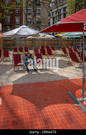 Paris, Frankreich - 08 27 2023: Strände Von Paris. Eine reife Frau, die auf einem Liegestuhl sitzt, unter einem weißen Sonnenschirm an den Kais des Bassin de la Villette Stockfoto