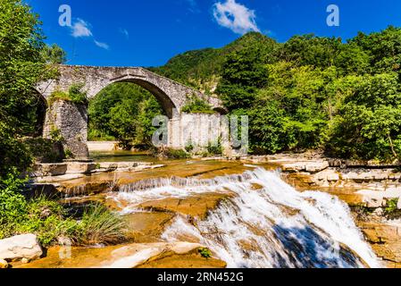 Die mittelalterliche Brücke Ponte della Brusia über den Fluss Fiume Montone und den Wasserfall in Bocconi in Emilia-Romagna, Italien Stockfoto