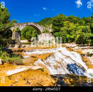 Panorama der mittelalterlichen Brücke Ponte della Brusia über den Fluss Fiume Montone und den Wasserfall in Bocconi in Emilia-Romagna, Italien Stockfoto