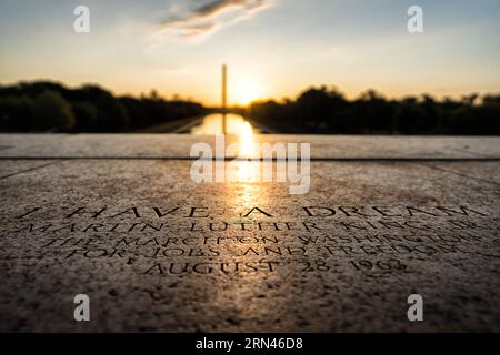 WASHINGTON DC, Vereinigte Staaten – das Washington Monument steht vor einem pulsierenden Sonnenaufgang, von den Stufen des Lincoln Memorial in Washington, DC. Genau an dieser Stelle auf den Stufen der Gedenkstätte hielt Martin Luther King Jr. seine berühmte Rede „Ich habe einen Traum“. ist mit einer Gravur der ikonischen Linie im Vordergrund gekennzeichnet. Stockfoto