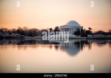 WASHINGTON DC, USA – das Jefferson Memorial reflektiert in den stillen Gewässern des Tidal Basin in den ruhigen Morgenstunden. Ein orangener Himmel deutet auf den nahenden Sonnenaufgang hinter der neoklassizistischen Kuppel und den Säulen der Gedenkstätte hin. Die ruhigen Bedingungen erzeugen spiegelartige Reflexionen auf der Wasseroberfläche. Stockfoto