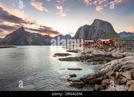 Rote Holzhütten, traditionelle rorbuer-Hütten, Fischerdorf Hamnoy bei Sonnenuntergang, felsige steile Berggipfel und Fjordlandschaft, Lofoten, Nordland Stockfoto