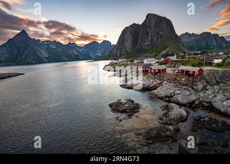 Rote Holzhütten, traditionelle rorbuer-Hütten, Fischerdorf Hamnoy bei Sonnenuntergang, felsige steile Berggipfel und Fjordlandschaft, Lofoten, Nordland Stockfoto