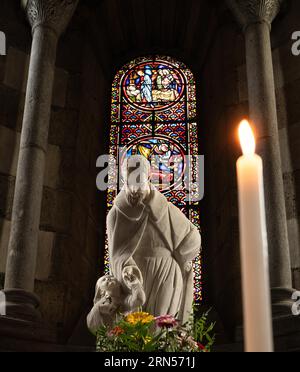 Innenaufnahme der heiligen Figur vor Buntglasfenster, Kerze, Kirche Saint Joseph, La Bourboule, Puy-de-Dome Departement Stockfoto