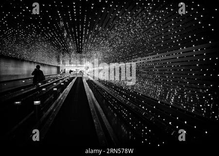 Fahrtreppenbeleuchtung, Stadt. Schwarzweiß-Foto, das die parallelen Lichtlinien zeigt, die in die Entfernung über der Rolltreppe zurückfallen. Stockfoto