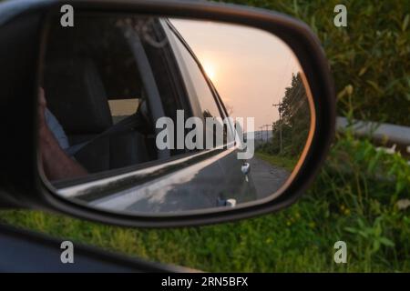 Reisefoto von der Abenteuerperspektive mit Autofahrten im Autospiegel mit Blick auf die untergehende Sonne Stockfoto