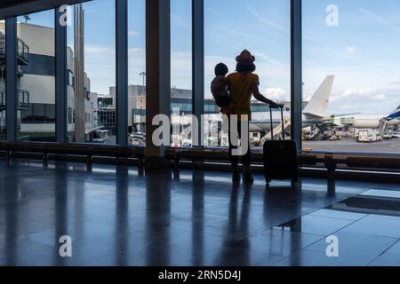 Mutter und Sohn mit Gepäck in der Nähe des Fensters und Blick auf die Flugzeuge im Flughafen Stockfoto