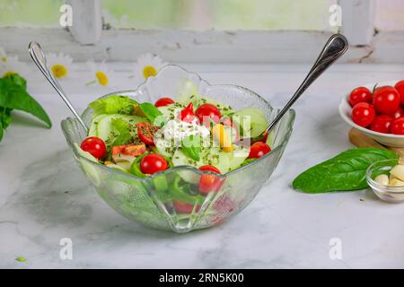 Gemischter Salat in Glasschüssel, Tomaten und Knoblauch daneben Stockfoto