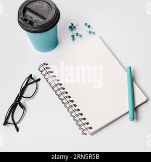 Einweg-Kaffeetasse Stift Brillen Spiral Notizblock Daumenstiften weißer Hintergrund Stockfoto