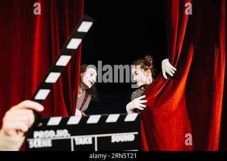 Person s Hand hält Klapperboard vorne zwei Pantomime Künstler Durchführung roten Vorhang Stockfoto