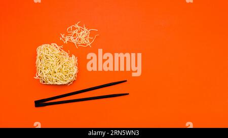 Gebrochene trockene Instant-Nudeln mit Essstäbchen orange Hintergrund Stockfoto