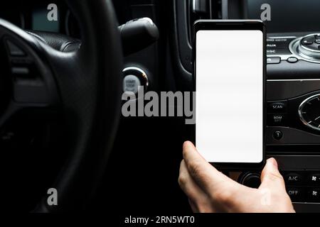 Nahaufnahme der Hand, die das Smartphone hält, zeigt das weiße Auto mit leerem Bildschirm Stockfoto
