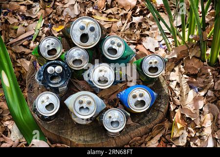 Aluminiumdosen mit Augen und offenem Mund in trockenen Blättern. Konzept des kreativen Recyclings. Verschiedene Farben und Größen, Konzept der Inklusivität Stockfoto