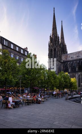 Menschen genießen den Sommer in Straßencafés und Restaurants, Place de la Victoire, dahinter Notre-Dame-de-l'Assomption Kathedrale, Clermont-Ferrand Stockfoto