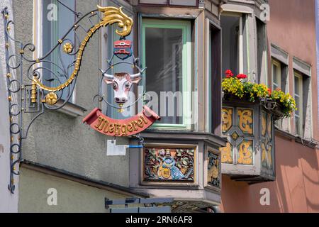 Erkerfenster (Bogenfenster) an alten Traditionshäusern im Schwarzwaldstil in der Altstadt und Nasenschild, gesticktes Schild mit Kuhkopfmotiv Stockfoto