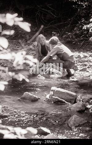 1970ER JAHRE ROMANTISCHES, JUNGES, LÄSSIGES PAAR, DAS IM WALDBACH KNIET - R23090 HAR001 HARS FRIENDSHIP HALF-LENGTH PERSONS STREAM EIN FÜRSORGLICHES TEENAGERMÄDCHEN TEENAGER BOY DENIM WANDERUNG B&W SOMMERZEIT DATING KNIEND GLÜCK HIGH ANGLE ABENTEUER FREIZEIT WATEN FREIZEIT ATTRAKTION BEZIEHUNGEN WADE CONNECTION BALZ TEENAGER PERSÖNLICHE BINDUNG MÖGLICHKEIT AFFEKTION BLAUE JEANS ZUSAMMENARBEIT EMOTION INFORMELLE ENTSPANNUNG SAISON SOZIALE AKTIVITÄT ZWEISAMKEIT TWILL WALD JUNGER ERWACHSENER MANN JUNGE ERWACHSENE FRAU JUGENDLICHE SCHWARZ-WEISS LÄSSIG KAUKASISCHE ETHNIE MIT HAR001 ALTMODISCH Stockfoto