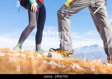 Männliche und weibliche Beine und Füße in den Sneakers, zwei Wanderer, die durch raues Berggelände mit hellem Himmel und Sonnenschein im Hintergrund laufen Stockfoto