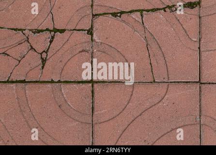 Nahaufnahme von gebrochenen und verwitterten roten quadratischen Pflastersteinen oder Blöcken mit geometrischen Formen im Freien, von oben gesehen. Texturierter Hintergrund im Vollformat. Stockfoto