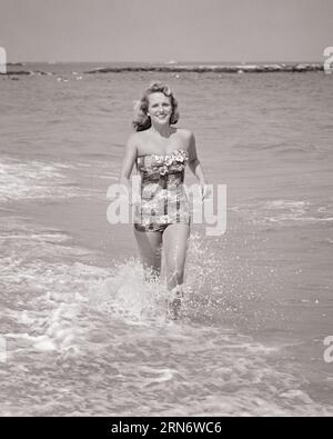 1950ER JAHRE LÄCHELNDE JUNGE FRAU MIT EINTEILIGEM TRÄGERLOSEN BADEANZUG, DER IN OZEANSURFEN LÄUFT UND DIE KAMERA ANSCHAUT - B8025 HAR001 HARS FRAUEN SCHWIMMEN GESUNDHEIT VEREINIGTE STAATEN KOPIEREN RAUM IN VOLLER LÄNGE DAMEN PERSONEN VEREINIGTE STAATEN VON AMERIKA SURF VERTRAUEN B&W NORDAMERIKA SOMMER AUGENKONTAKT FREIHEIT NORDAMERIKA ZEIT ABSEITS DER KÜSTE GLÜCK FRÖHLICHES ABENTEUER FREIZEIT URLAUB SPANNUNG ERHOLUNG STOLZ STRÄNDE URLAUB LÄCHELN TRÄGERLOSE SCHWIMMER EINTEILIGE FLUCHT FRÖHLICHER SAND STILVOLL ENTLANG DER KÜSTE NEW JERSEY SAISON URLAUB JUNGE ERWACHSENE FRAU SCHWARZ-WEISS KAUKASISCHE ETHNIZITÄT HAR001 ALTMODISCH Stockfoto