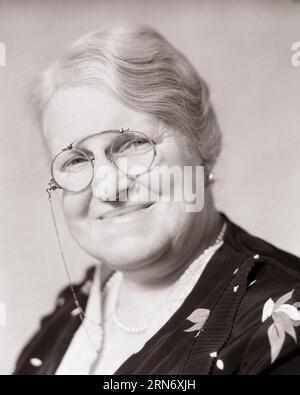 1930ER JAHRE PORTRÄT EINER LÄCHELNDEN SENIORIN, DIE PINCE-NEZ AN EINER KETTE TRÄGT, DIE AUF DIE KAMERA SCHAUT - S. 3907 HAR001 HARS GRANDPARENT STUDIO SHOT CHAIN COPY SPACE DAMEN PERSONEN OHRRINGE VERTRAUEN BRILLEN SENIOR ERWACHSENE AUSDRÜCKE SCHWARZWEISS AUGENKONTAKT SENIOR FRAU VISION GLÜCK ALT ALTER OLDTIMER KOPF UND SCHULTERN FRÖHLICHER OLDSTER STOLZ PINCE-NEZ GROSSMÜTTER LÄCHELT ÄLTESTE FRÖHLICH, STILVOLL, AUFRICHTIG, ANGENEHM, SCHWARZ UND WEISS KAUKASISCHE ETHNIZITÄT ERNSTE GROSSMUTTER HAR001 ALTMODISCH Stockfoto