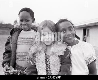 1970ER-JAHRE-KLASSENKAMERADEN AFROAMERIKANISCHER JUNGE UND MÄDCHEN MIT EINEM KAUKASISCHEN MÄDCHEN POSIERTEN ZUSAMMEN UND SCHAUTEN LÄCHELND AUF DIE KAMERA - J14361 HAR001 HARS ELEMENTARER STIL VIELSEITIGER FREUND VERSCHIEDENE FREUDE LIFESTYLE FRAUEN GEWINNEN KOPIE RAUM FREUNDSCHAFT HALBE LÄNGE MÄNNER SELBSTVERTRAUEN B&W AUGEN KONTAKT SCHULEN KLASSE GLÜCK FRÖHLICH AFROAMERIKANER AFROAMERIKANER UND SCHWARZE ETHNIZITÄT STOLZ PRIMÄR LÄCHELT VERBINDUNG FREUNDLICH FREUDIG VERSCHIEDENE ANGENEHM ABWECHSLUNGSREICH ANGENEHM CHARMANT GRAD SCHULWUCHS JUGENDLICHE LIEBENSWERT ANSPRECHEND POSIERTE VOR-TEENAGER-MÄDCHEN ZWEISAMKEIT ENTZÜCKEND ANSPRECHEND SCHWARZ-WEISS KAUKASISCHE ETHNIE Stockfoto