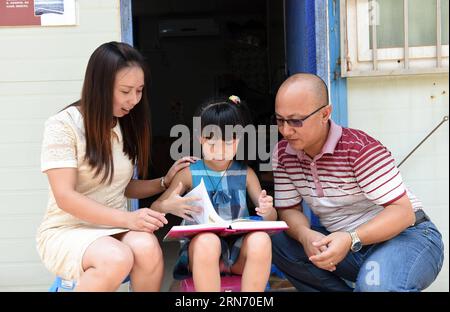 (150812) -- NANNING, 12. August 2015 -- das 8-jährige Mädchen Zhou Panni, das aus dem südwestchinesischen Chongqing kommt, liest mit ihren Eltern auf einer Baustelle in Nanning, der Hauptstadt der südchinesischen autonomen Region Guangxi Zhuang, 12. August 2015. Fast eintausend Bauarbeiter aus dem ganzen Land arbeiten auf der Baustelle der Lianqing Bridge in Nanning City, weit weg von ihren Kindern und ihrem Zuhause. Einige Kinder können nicht bis zum Frühlingsfest warten, das einzige Mal, dass ihre Eltern nach Hause zurückkehren, kamen aber während ihres Sommerurlaubs nach Nanning, um sich wiederzusehen.) (MT) CHINA-NANNING-BAUSTELLENFAMIL Stockfoto