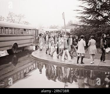 1970ER-JAHRE GRUPPEN VON SCHÜLERN, DIE SCHULBUSSE AUF EINEM REGNERISCHEN, NASSEN BÜRGERSTEIG VERLASSEN - S18718 HAR001 HARS-LEHRERINFORMATIONEN LIFESTYLE FRAUEN KOPIEREN RAUM FREUNDSCHAFT IN VOLLER LÄNGE REGNERISCHE PERSONEN MÄNNER TEENAGER MÄDCHEN REGEN TEENAGER JUNGEN B&W SCHULEN ABENTEUER LEHRER WISSEN GELEGENHEIT HIGH SCHOOL ZU HIGH SCHOOL VERBINDUNG EXKURSIONSLEHRER JUGENDBUSSE ZUSAMMENARBEIT PÄDAGOGEN LEHRER JUGENDLICHE SCHULE LEHRT ZWEISAMKEIT SCHWARZ UND WEISSE KAUKASISCHE ETHNIE, DIE AUS DER HAR001-TRADITION AUSGEHT Stockfoto