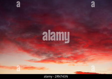 Sonnenuntergang mit Licht, das sich in Wolken spiegelt. Strukturierter Hintergrund mit wunderschönem Sonnenuntergang. Erstaunlicher rot-gelber Sonnenuntergang mit „brennenden Wolken“ Panoramablick Sonnenuntergang Stockfoto