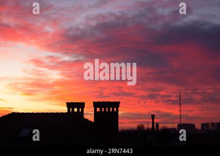 Erstaunlicher rot-gelber Sonnenuntergang mit „brennenden Wolken“ und kontrastreichem Horizont der Skyline der Stadt. Panorama Sonnenuntergang Wolkenlandschaft dramatischer Himmel Stadtbild Stockfoto