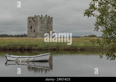 Blick über einen See auf ein verlassenes Schloss mit einem weißen Ruderboot im Wasser Stockfoto