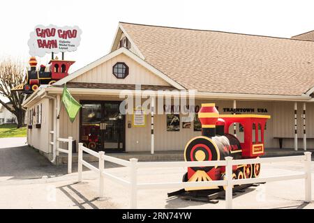 Choo Choo Barn Außeneingang Strasburg Pennsylvania Frühling | STRASBURG, Pennsylvania — Der Außeneingang des Choo Choo Barns kündigt sich mit einem wolkenförmigen Schild mit der Aufschrift „Gigantisches Modellzuglayout“ und einer großen dekorativen Dampflokomotive, die über dem Eingang thront, sowie einer fahrbaren Miniaturzug im Vorhof an. Die Attraktion wird seit ihrer Eröffnung durch die Familie Groff im Jahr 1961 in Strasburgs Schienentourismus-Korridor betrieben, der auch die Strasburg Rail Road und das Railroad Museum von Pennsylvania beherbergt, und ist damit eine der längsten Modellzug-Attraktionen in den Vereinigten Staaten Stockfoto