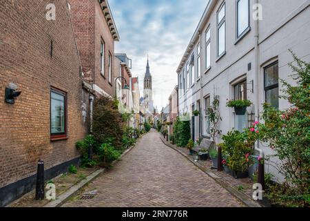 Malerisches Delfter Stadtbild mit Blick durch eine enge alte Gasse auf dem Turm des berühmten Nieuwe Kerk. Delft, Niederlande. Alte Gasse calle Stockfoto