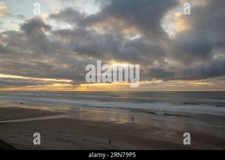 Menschen, die am Strand in Lincoln City, Oregon, spazieren gehen, während der Sonnenuntergang von der Neptune Suite im Starfish Manor aus gesehen wird Stockfoto
