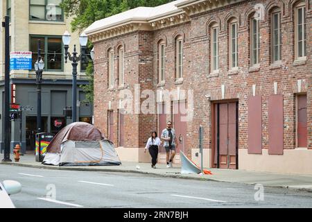 Ein Paar, das an einem Zelt eines Obdachlosen in der Innenstadt von Portland, Oregon, vorbeiläuft Stockfoto