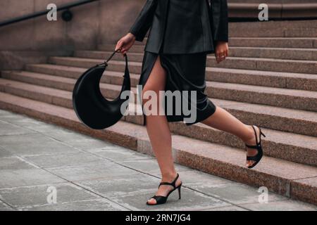 Modische Details eines schwarzen Lederrock, einer Jacke und einer Handtasche. Eine Frau, die in der Stadt spaziert. Stoffkonzept im Straßenstil Stockfoto