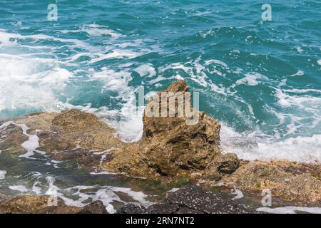 Wellen am felsigen Strand in Griechenland. Sommertag mit rauem Meer. Stockfoto