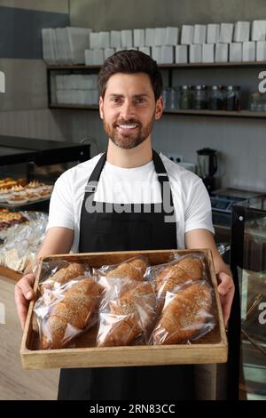 Glücklicher Verkäufer, der ein Tablett mit leckeren Croissants in der Bäckerei hält Stockfoto