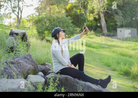 Frau, die ein Selfie macht, sitzt auf einem Felsen mitten in der Natur. Stockfoto