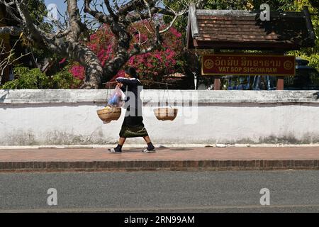 Eine laotische Frau, die auf der Straße vor einem Tempel in Luang Prabang, Laos, spaziert Stockfoto