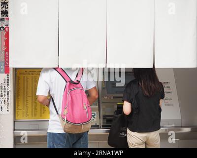 TOKIO, JAPAN - 27. August 2023: Menschen, die Fahrkartenautomaten hinter einem norenförmigen Vorhang am Bahnhof Ochanomizu benutzen. Stockfoto