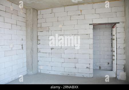 Neue Wohnung mit Porenbetonblockwänden, Betondecke, Säule und Tür in einem neuen Wohngebäude ohne Verputz. Stockfoto