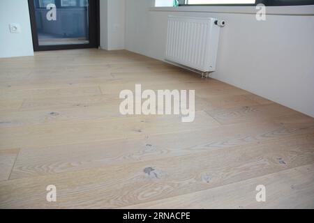 Nahaufnahme auf dem Holzfußboden des Hauses mit Heizkörperheizung in einem modernen leeren Raum. Stockfoto