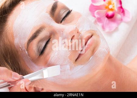 Zugeschnittenes Bild der Kosmetikerin, die Maske auf das Gesicht des Kunden im Salon Stockfoto