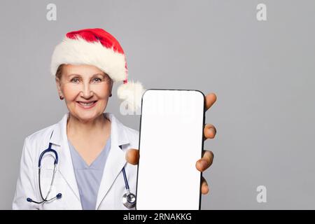 Weihnachtsporträt der lächelnden Ärztin in Santa hat mit Smartphone mit leerem weißen Bildschirm für neue Anwendung oder mobile Website Stockfoto