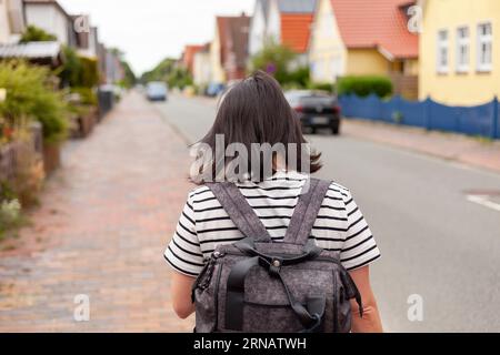 Ein Mädchen in einem gestreiften T-Shirt und einem Rucksack spaziert durch die Straßen einer Küstenstadt. Reisender im Urlaub in Europa. Rückansicht Foto Stockfoto