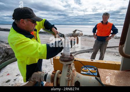 Salzbergleute, die Wasser zwischen Verdunstungsteichen bei der WA Salt Supply Company in Lake Deborah, Western Australia, pumpen Stockfoto